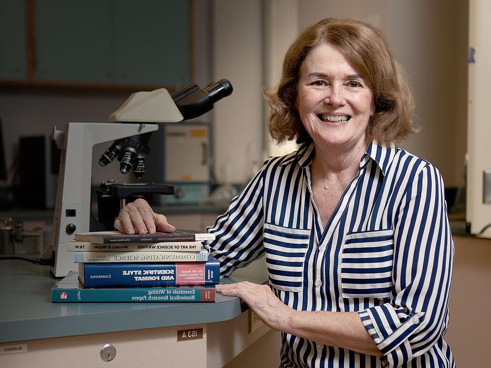 Portrait of Susan Gardner in front of microscope and stack of writing textbooks