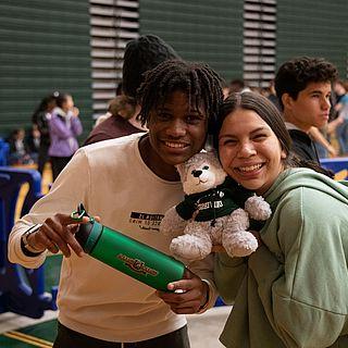 一名男学生和一名女学生站在一起，手里拿着WWU的商品. 他们对着镜头微笑.